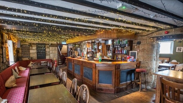 A cozy bar with wooden furniture, a stone wall, and string lights.