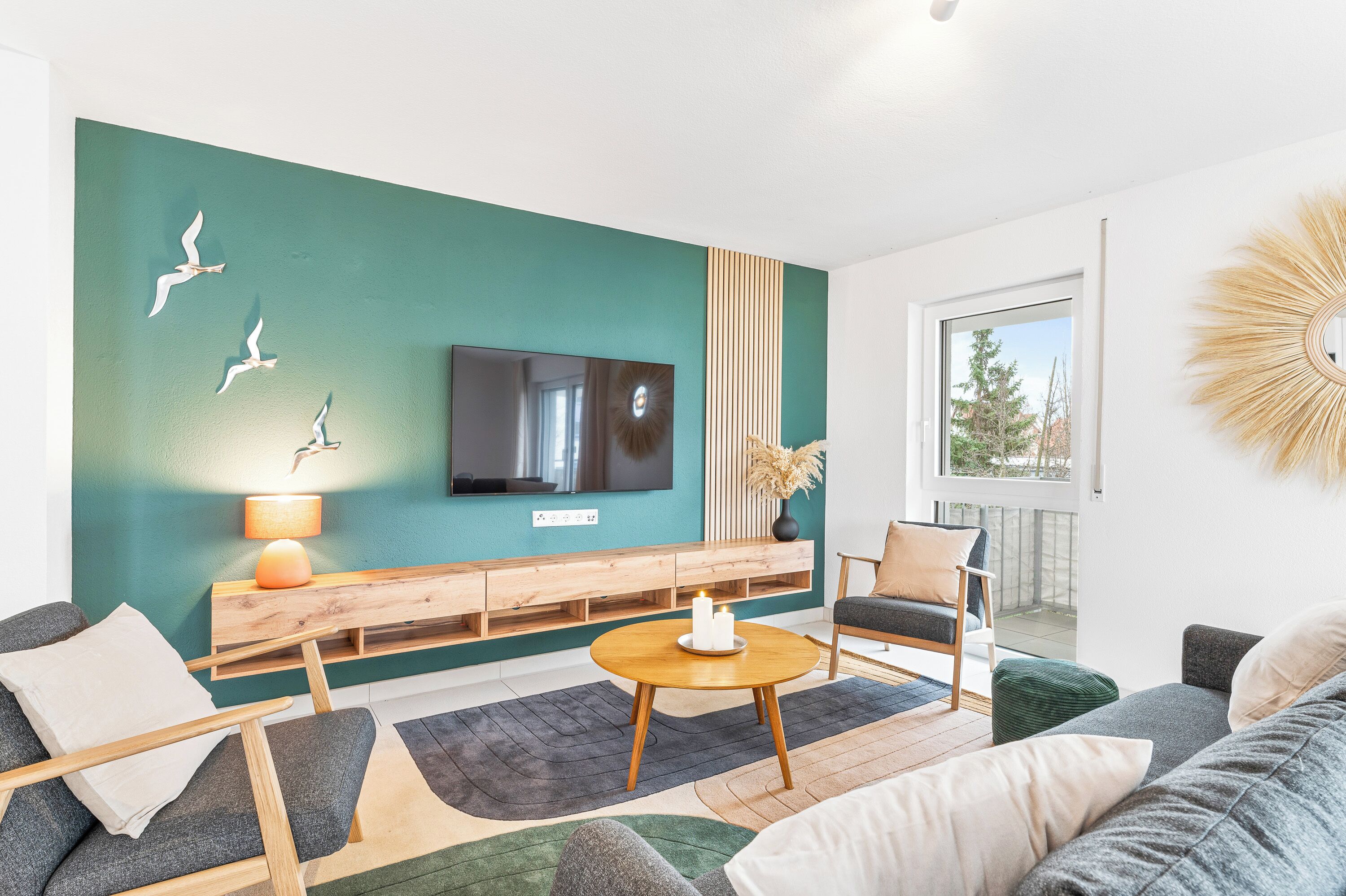 Ein modernes Wohnzimmer mit einer türkisfarbenen Akzentwand, einem Flachbildfernseher, einer Holzbank und Blick ins Freie.