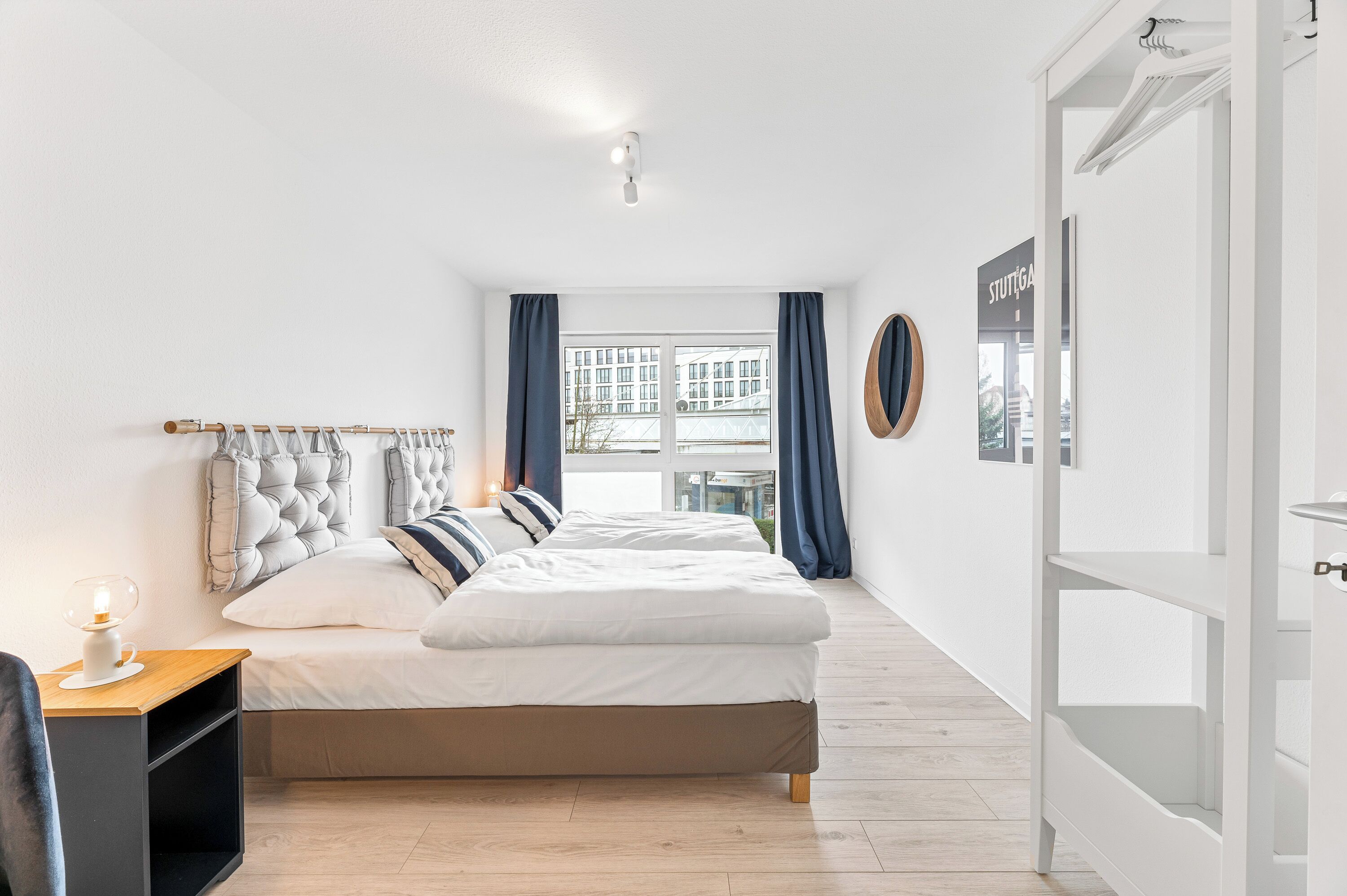 Une chambre moderne avec un grand lit, une table de chevet avec une lampe et une vue sur la ville par la fenêtre.