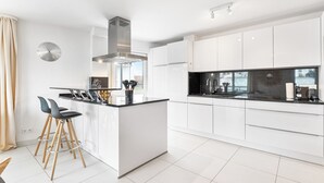 A modern kitchen with white cabinetry, a central island with stools, and a stainless steel range hood. - Design apartment near Stuttgart/Airport (Leinfelden-Echterdingen)