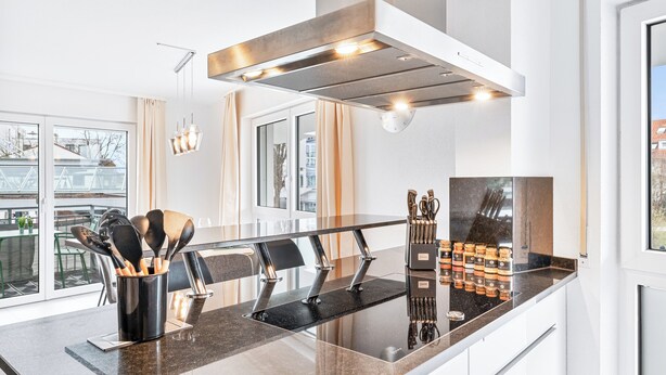 A modern kitchen with a stainless steel range hood, a black granite countertop, and a set of knives and spoons in a holder. - Design apartment near Stuttgart/Airport (Leinfelden-Echterdingen)