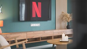 A modern interior with a flat-screen TV mounted on a teal wall, wooden furniture, and a vase with dried plants. - Design apartment near Stuttgart/Airport (Leinfelden-Echterdingen)