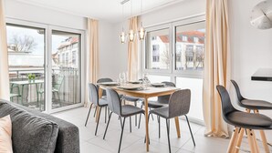 A modern dining area with a wooden table, grey chairs, and a glass partition. - Design apartment near Stuttgart/Airport (Leinfelden-Echterdingen)