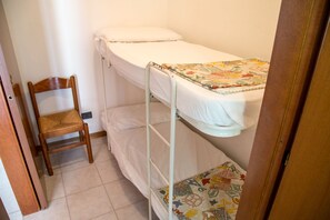 Une petite chambre avec un lit simple et un lit superposé, une chaise en bois et une couvre-lit à motifs.