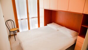 A bedroom with a bed, a chair, and a window with curtains. - Family Flat With two Private Courtyards (Eraclea)