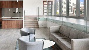 A modern interior with a sofa, chairs, a small table, a kitchen area, and a staircase. - Oceana Suites Irarrazaval (Santiago)