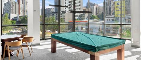 A pool table in a room with large windows overlooking a cityscape.