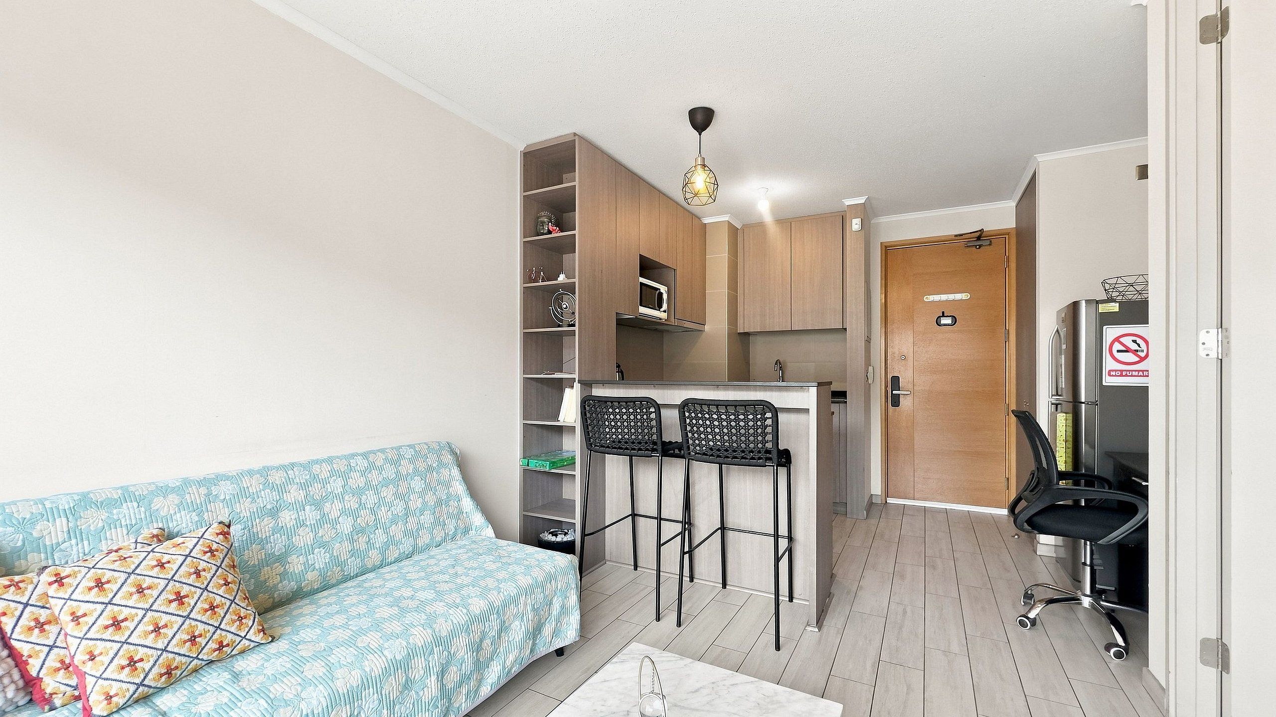 Un espace de vie compact comprenant un canapé, une kitchenette et une porte sur laquelle est apposé un panneau « Il est interdit de fumer ».
