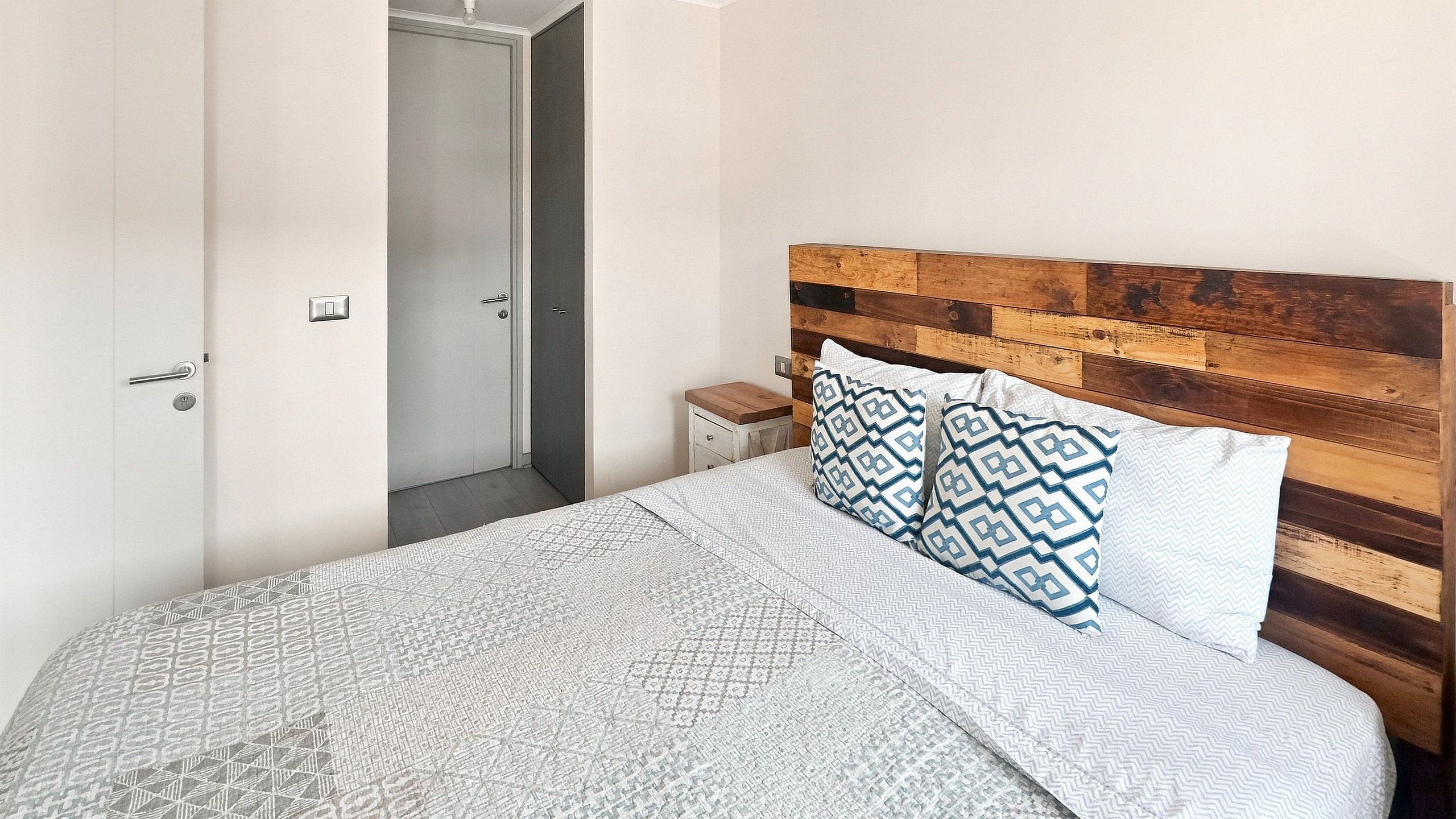 A bedroom with a bed, a wooden headboard, a nightstand, and a door.