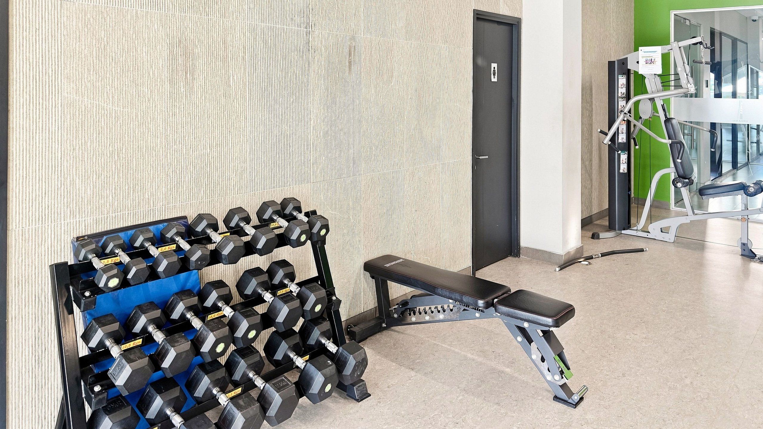Un gimnasio con una barra de mancuernas, una banca y equipo de ejercicio.