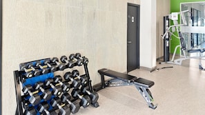 Une salle de sport équipée d’un porte-haltères, d’un banc et de divers appareils d’exercice.