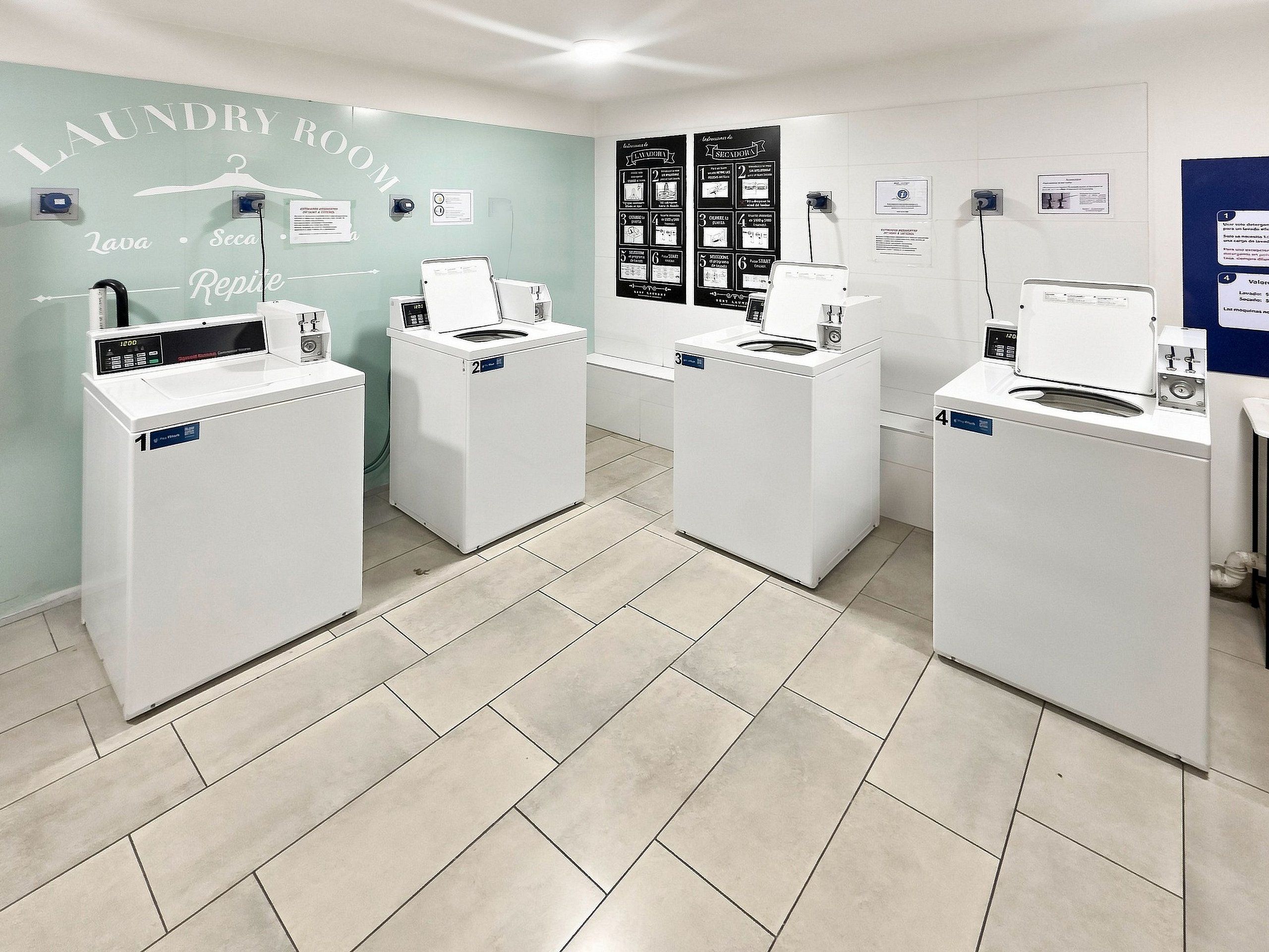A laundry room with four washing machines, a wall-mounted drying rack, and instructional posters.