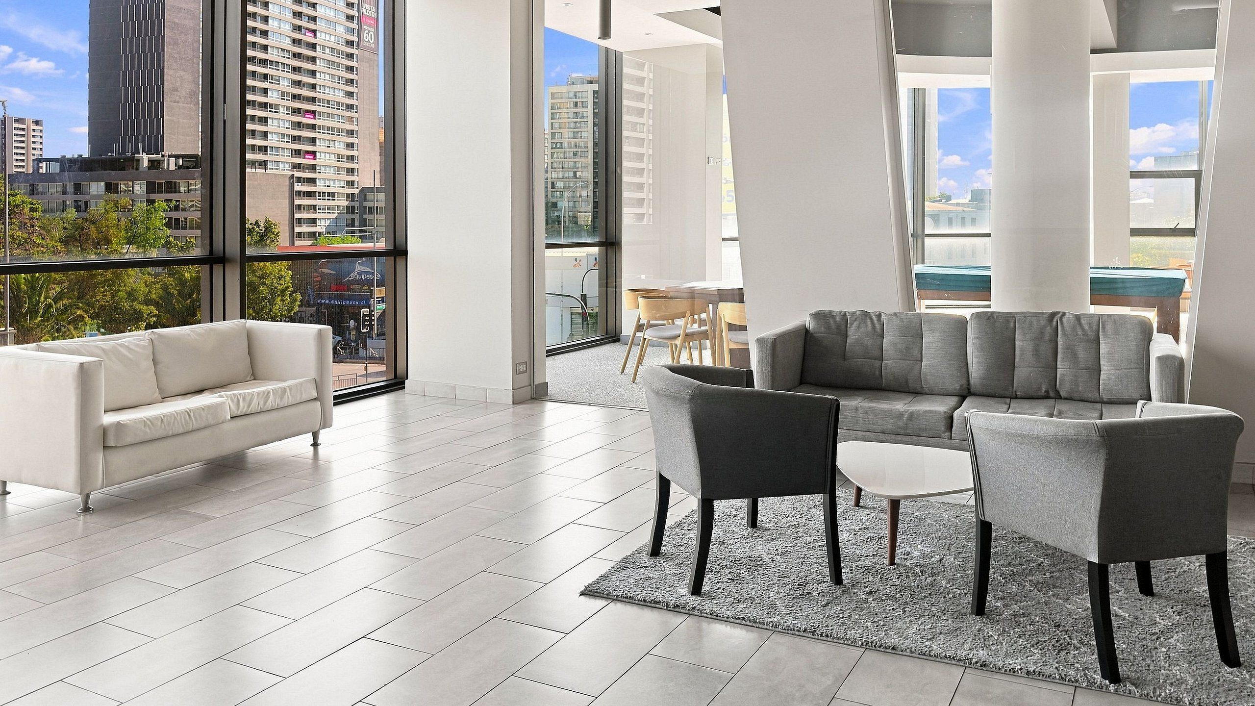 A spacious living area with a white sofa, grey armchairs, and a grey sectional sofa.
