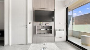 A modern living room with a flat-screen TV mounted on the wall, a small shelf with a picture frame, and a glass door leading to an outdoor balcony. - Oceana Suites Irarrazaval (Santiago)