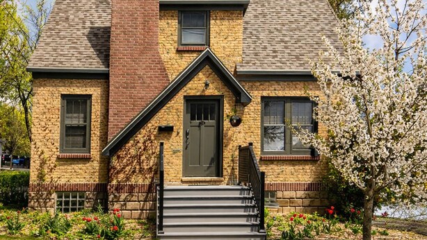 A two-story house with a brick chimney, a front porch with steps, and a small garden with flowers.