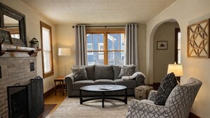 A living room with a sofa, armchair, coffee table, fireplace, and large windows.