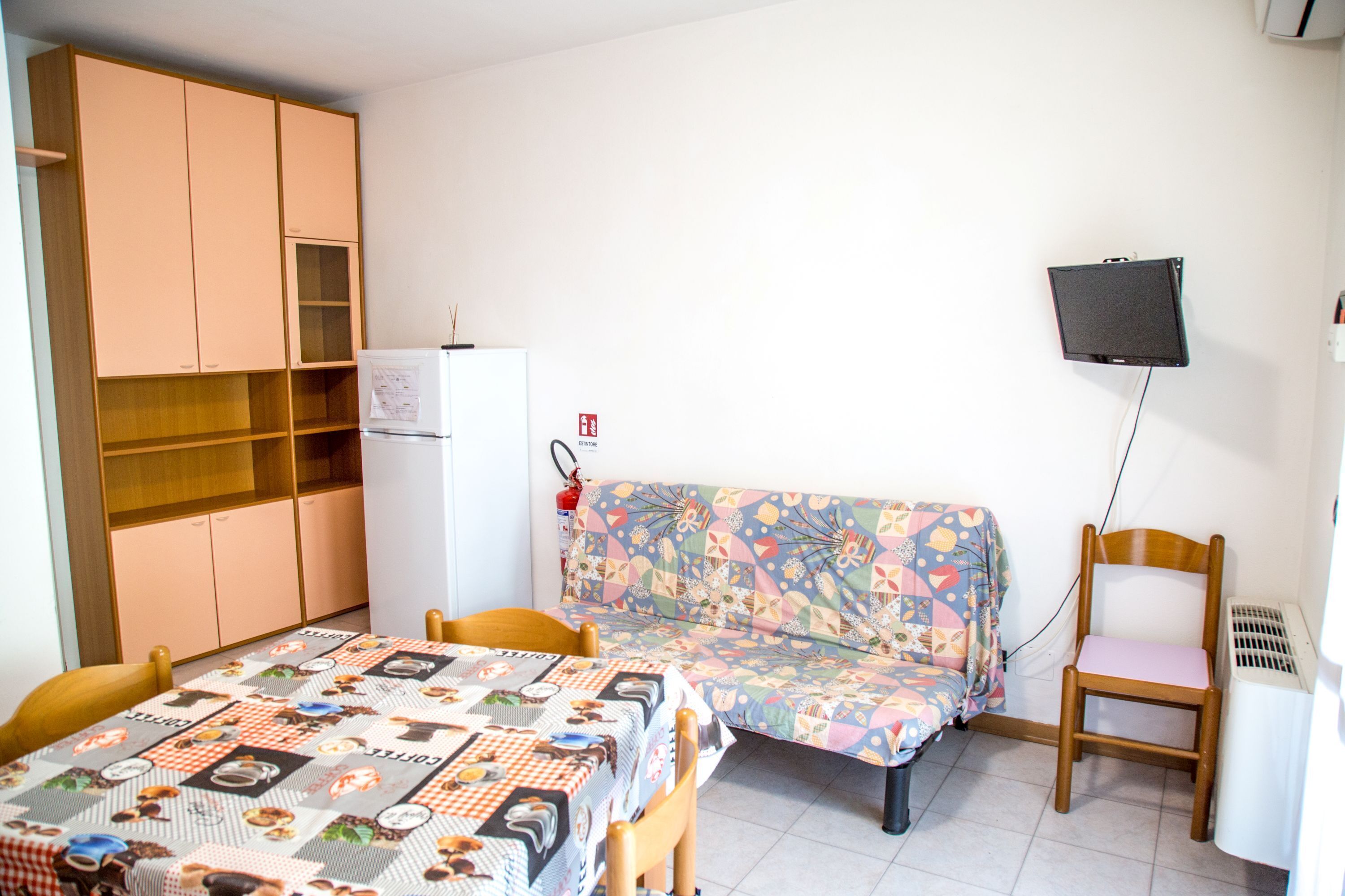 Une petite pièce comprenant un lit, un canapé, une chaise, une télévision et un réfrigérateur.