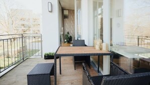 A balcony with a wooden table and black wicker furniture, a glass railing, and a view of the outdoors. - 2 room apartment in Hamburg for 6 people (Hamburg)