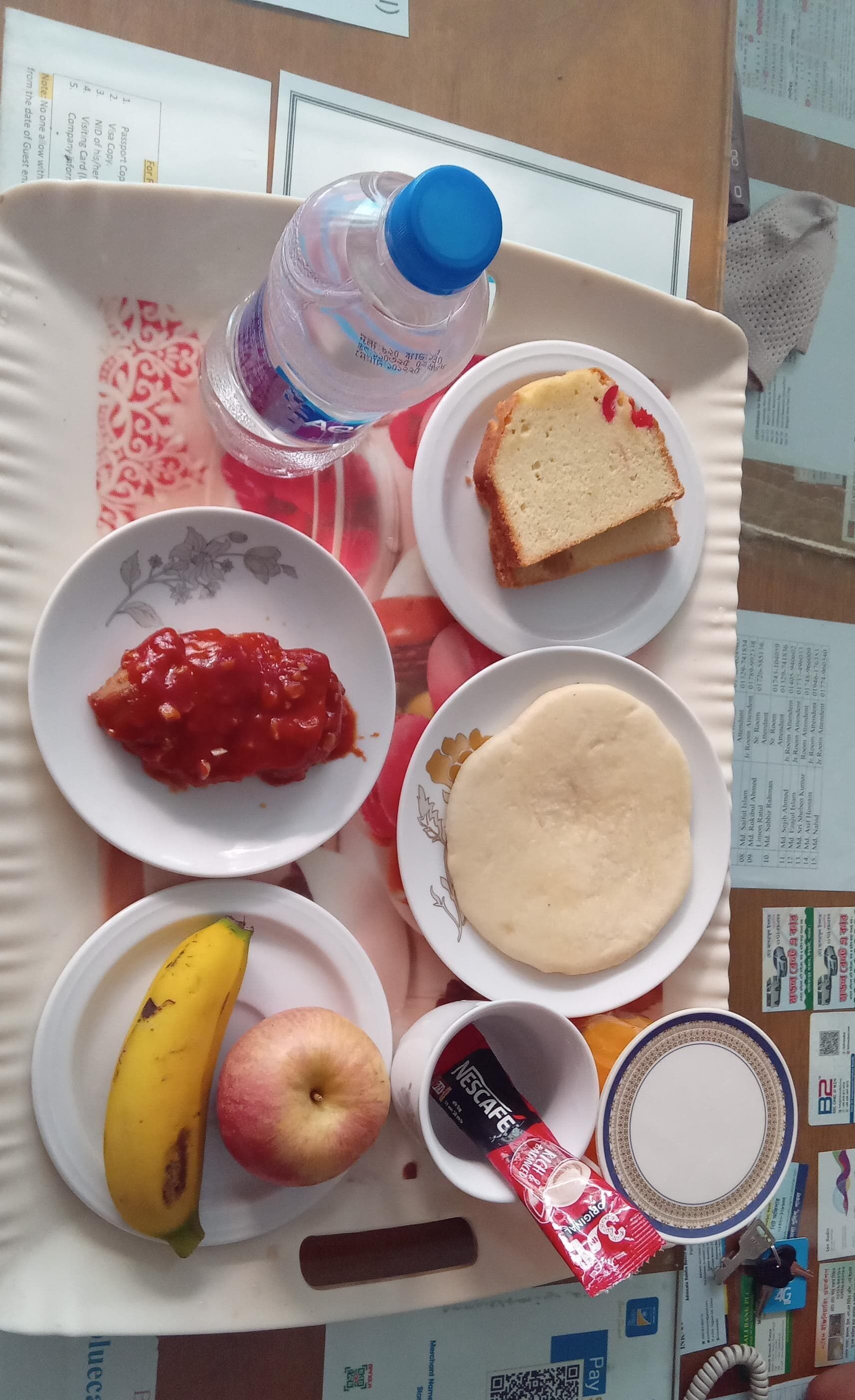 A tray with food items including bread, tomato sauce, a banana, an apple, and a Nescafe cup.