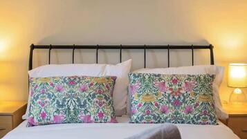 A neatly made bed with floral pillows, a green throw blanket, and a painting above.