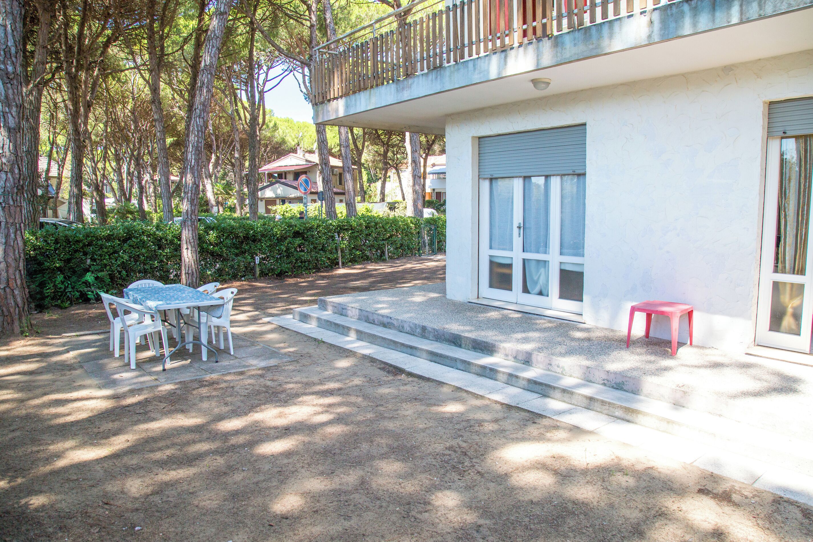 A building with a balcony, a table with chairs, and a red stool.