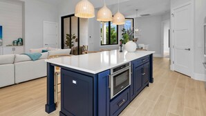 Uma cozinha moderna com ilha central, armários azul escuro e eletrodomésticos de aço inoxidável, com iluminação pendente.