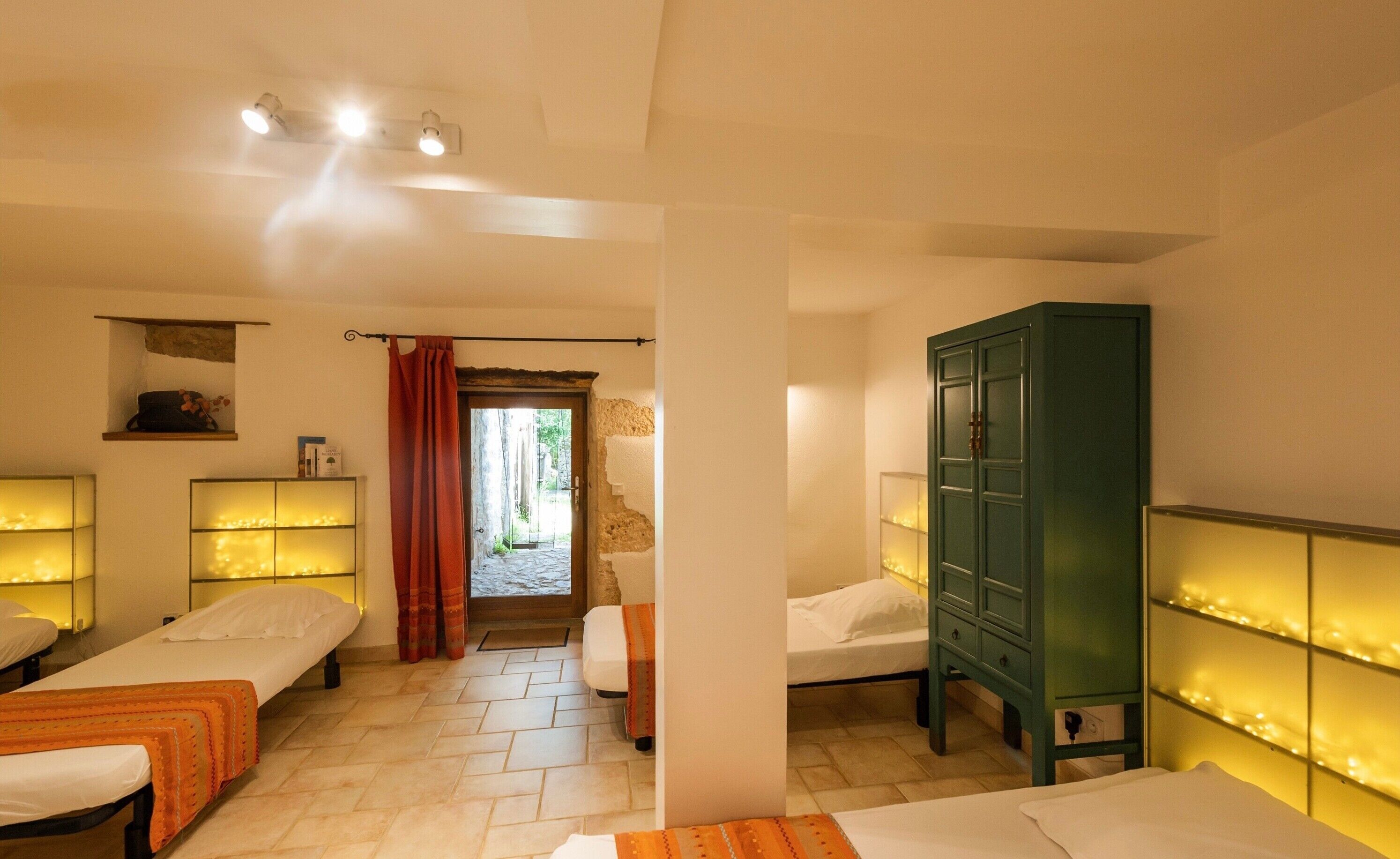 Ein Hotelzimmer mit zwei Betten, einem grünen Schrank, einer kleinen Bücherablage und Blick auf einen Innenhof.