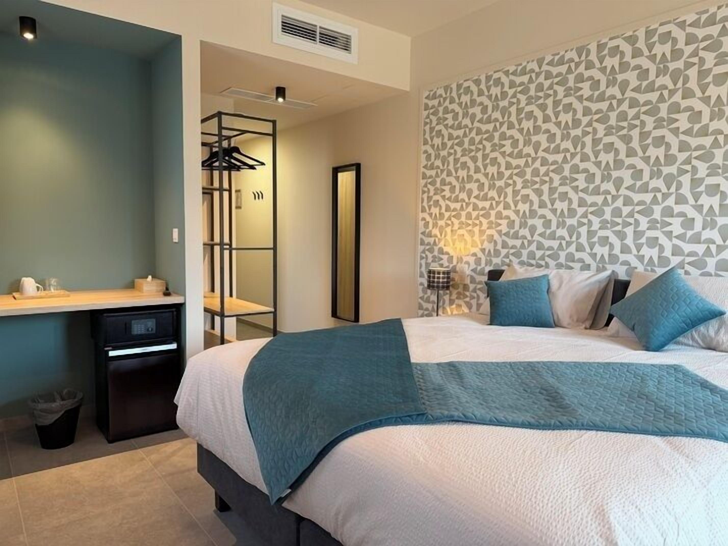 A modern bedroom with a large bed, a desk with a chair, and a wardrobe.
