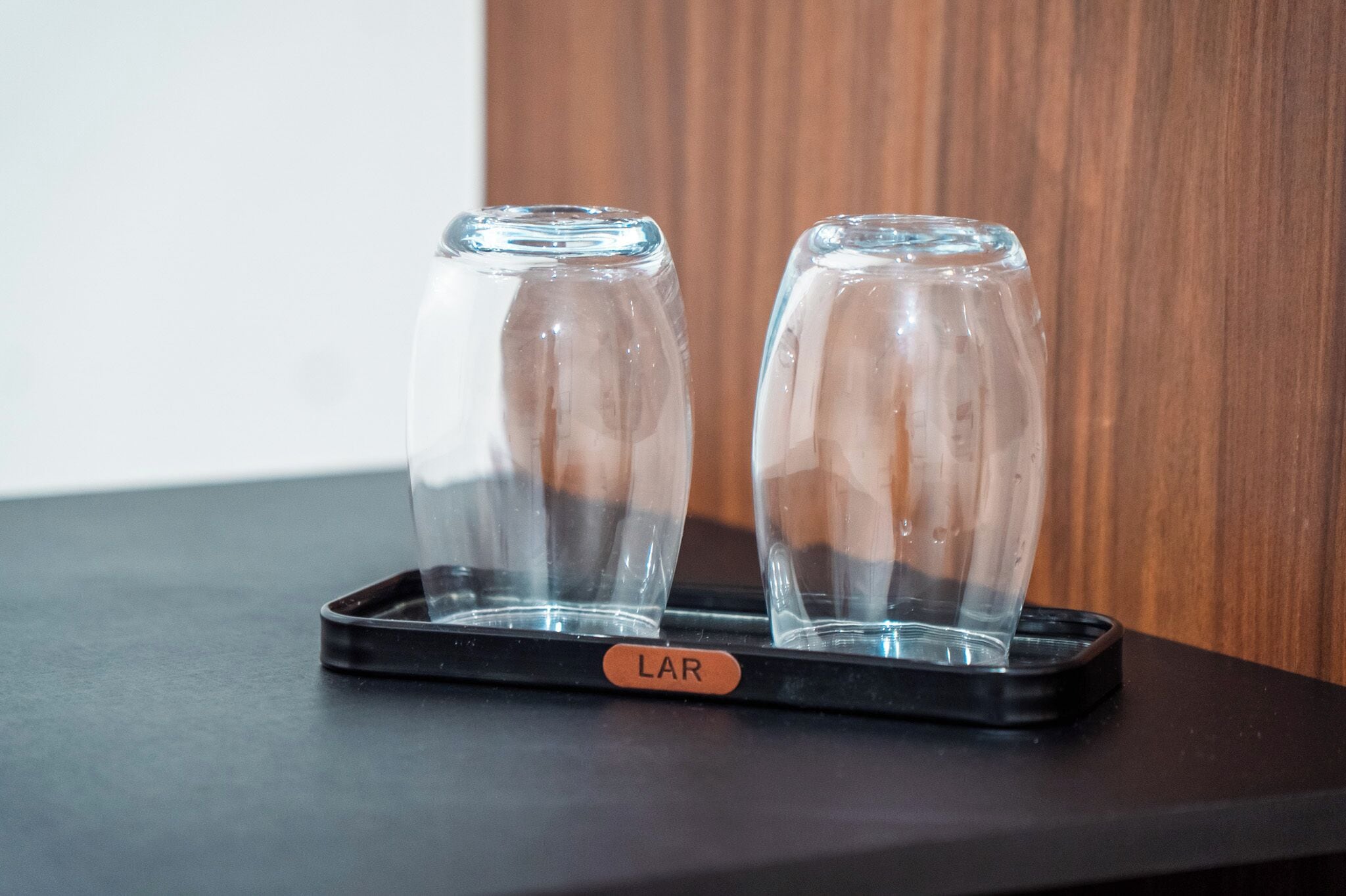 Two clear glasses on a black tray with a label 'LAR' on a table against a wooden background.