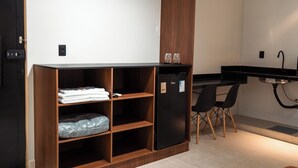 Een kitchenette met een zwarte koelkast, houten planken, een zwart aanrecht en twee zwarte stoelen.