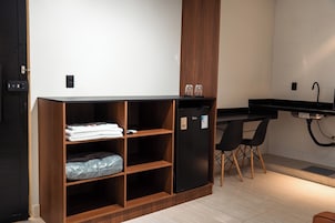Una kitchenette con un refrigerador negro, estantes de madera, una cubierta de mostrador negra y dos sillas negras.