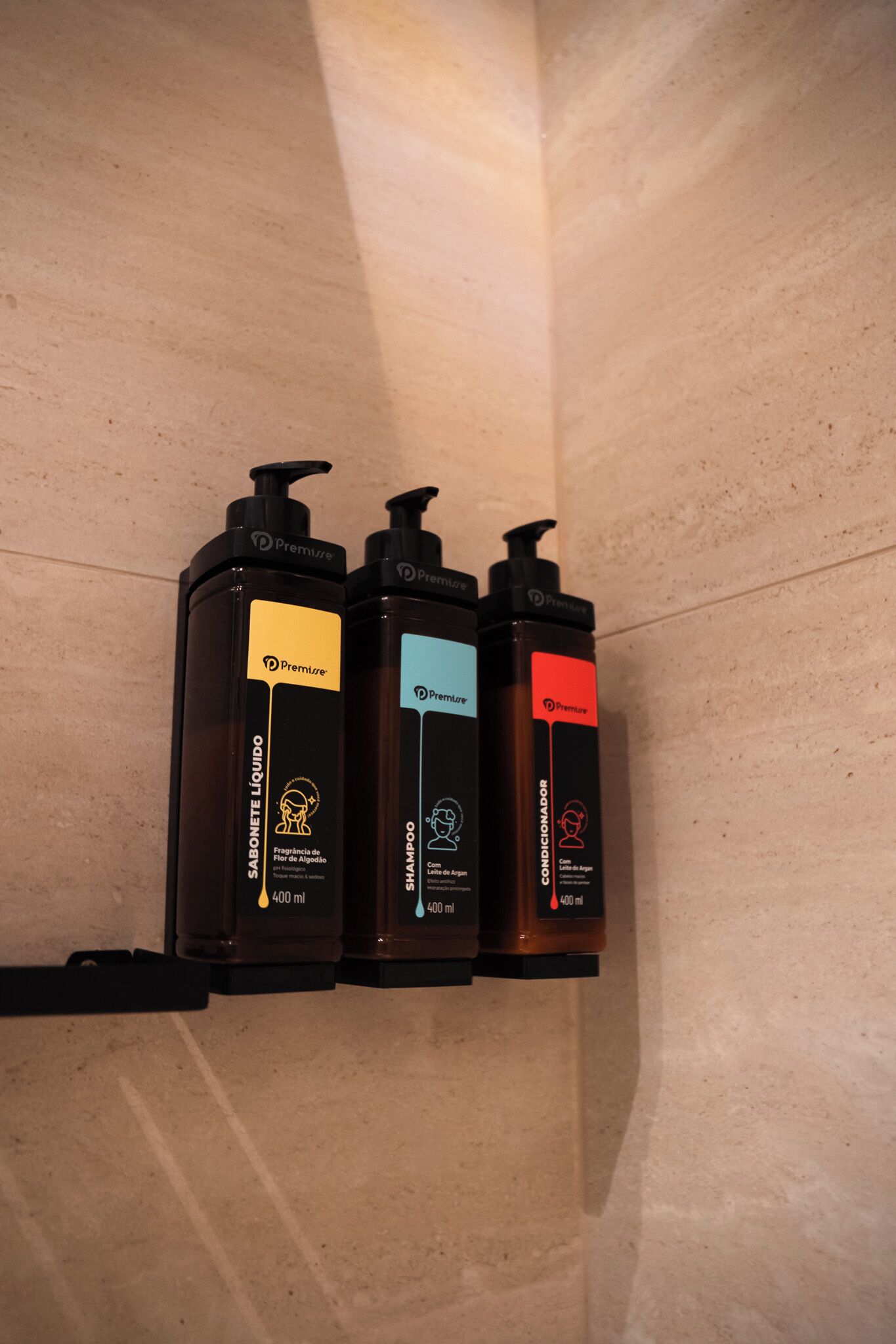 Three black Premier toiletries dispensers on a beige wall.