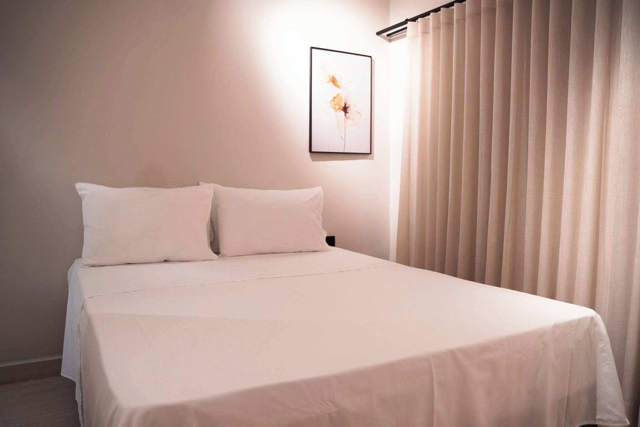 Una cama bien hecha con ropa blanca, un cuadro en la pared y una ventana con cortinas.