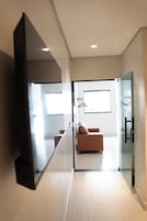Habitación de hotel moderna con un televisor de pantalla plana grande, un sofá, una ventana y un separador de vidrio.
