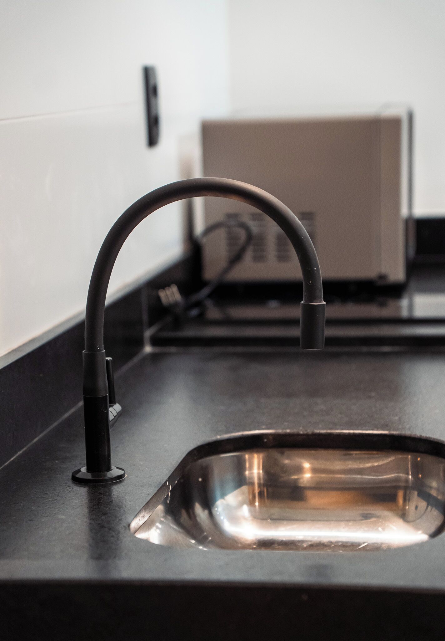 Cozinha com bancada preta, pia de aço inoxidável e torneira preta.