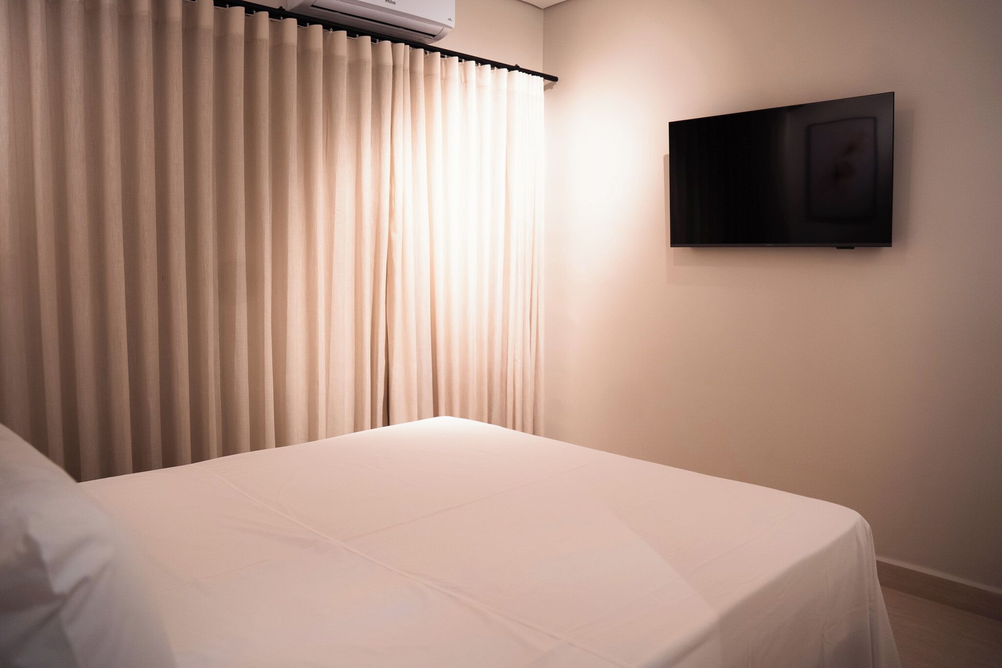A hotel room with a bed, curtains, and a mounted television.