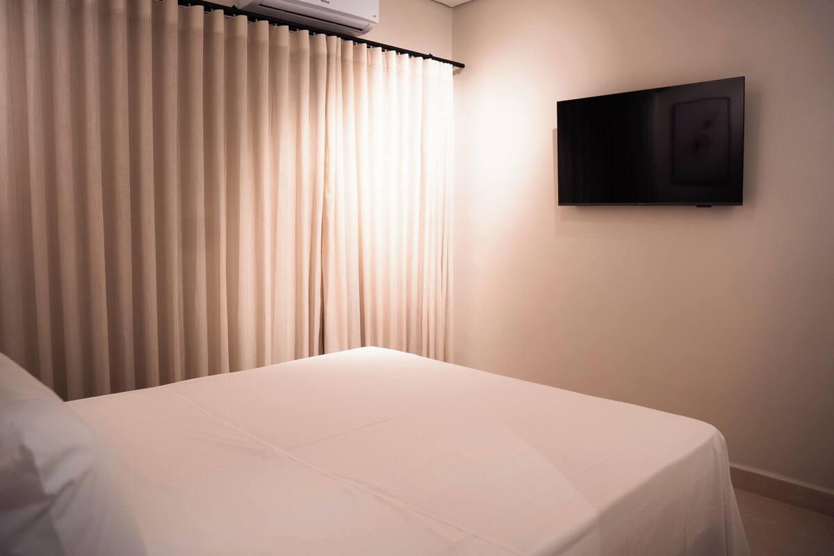 Una habitación de hotel con cama, cortinas y televisor de pared.