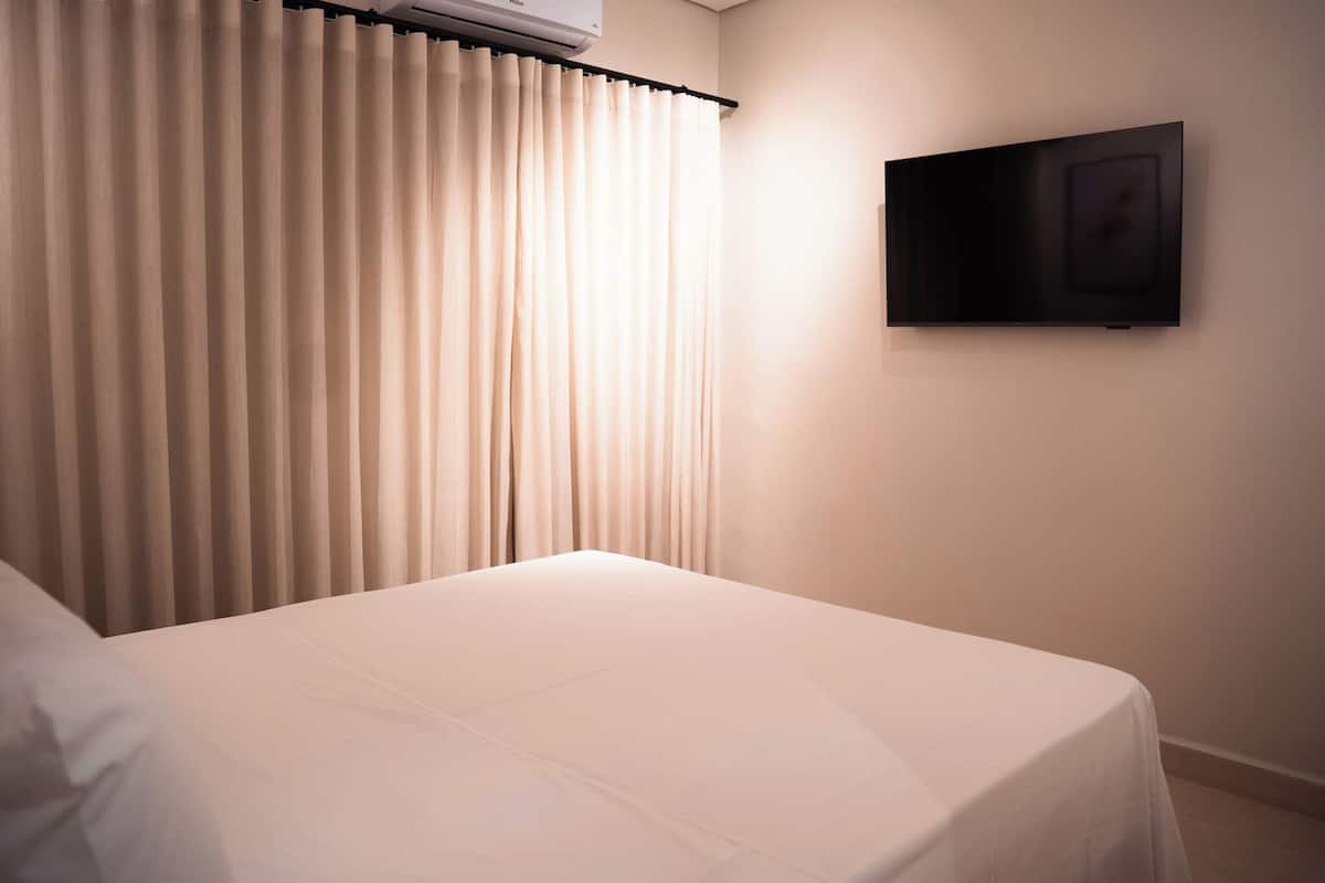 A hotel room with a bed, curtains, and a mounted television.
