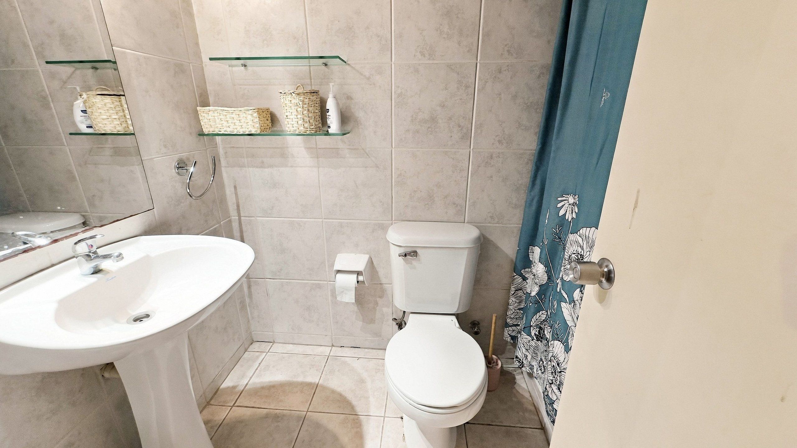 Een badkamer met een wit wastafel, toilet en een glazen plank met toiletartikelen.