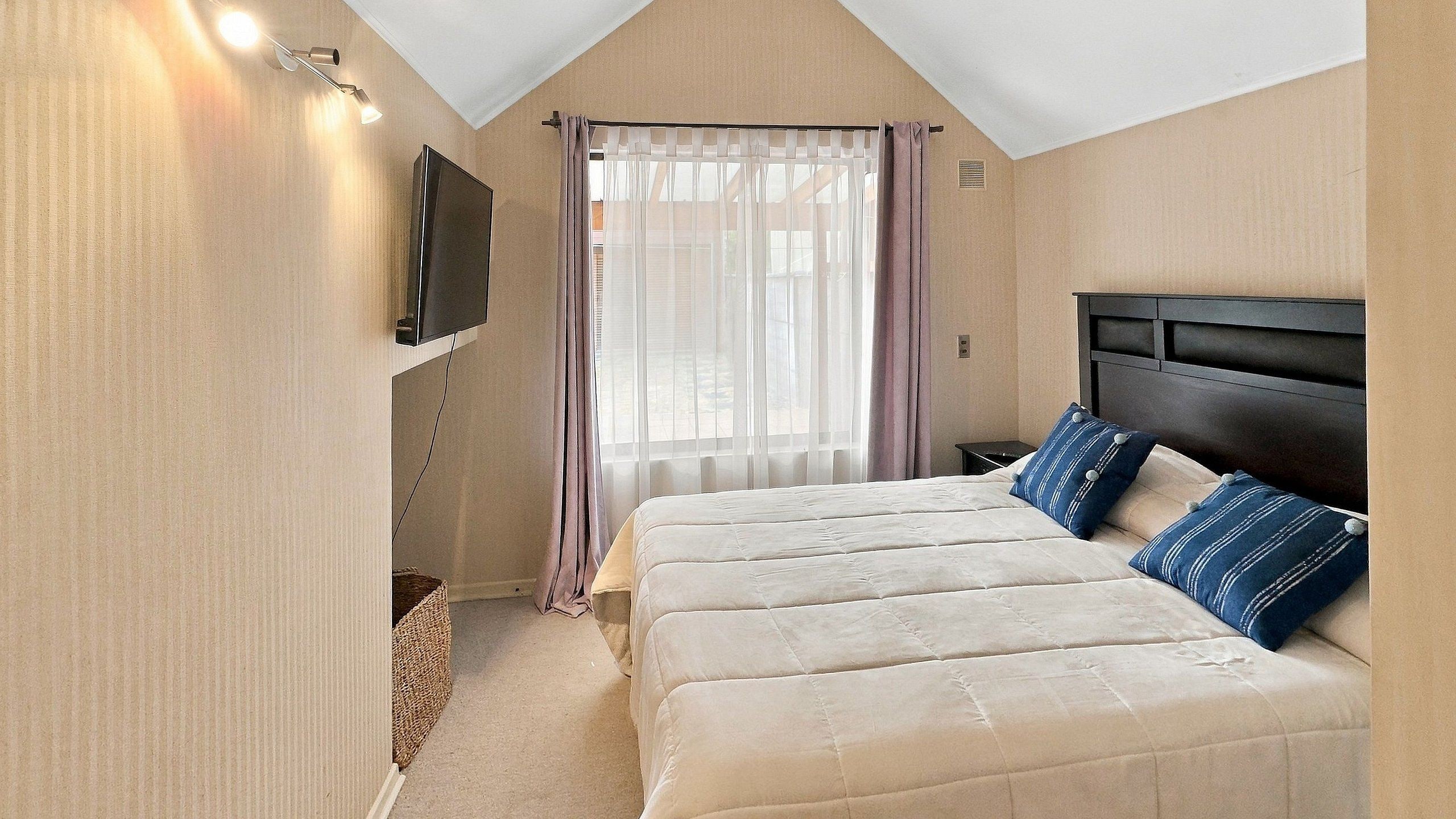 A bedroom with a large bed, a television mounted on the wall, and a window with curtains.