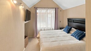 Une chambre avec un grand lit, un téléviseur fixé au mur et une fenêtre avec des rideaux.