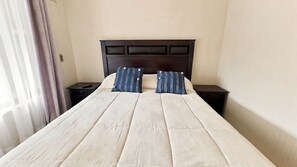 Habitación de hotel con una cama grande, dos mesitas de noche, un cabecero oscuro y una ventana con cortinas.