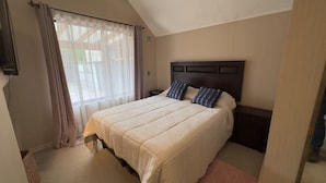 A bedroom with a large bed, a dark headboard, and a window with sheer curtains. - Oceana Suites Los Maticos (Puerto Montt)