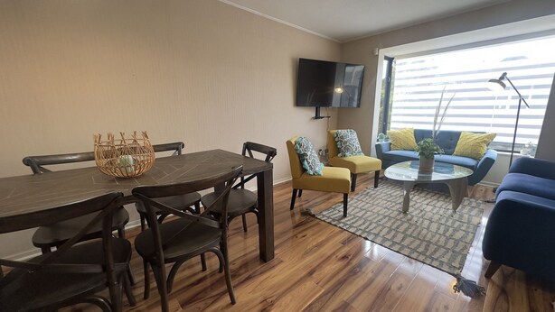A modern living room with a wooden dining table, chairs, a sofa, and a coffee table. - Oceana Suites Los Maticos (Puerto Montt)