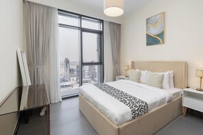 A hotel room with a large bed, two bedside tables, a painting on the wall, and a view of a cityscape through a large window. - Vogue | Creek Edge Creek Harbor Waterfront Living (Dubai)