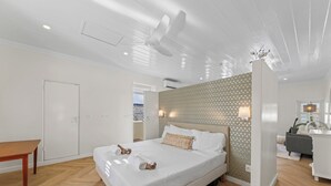 Moderni hotellihuone, jossa on suuri sänky, puulattia, kattotuuletin ja kuvioitu seinä.