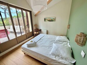 Ein Schlafzimmer mit einem großen Bett, Blick ins Freie durch eine Schiebetür, einem Sessel, einem Tisch und einem Gemälde an der Wand.