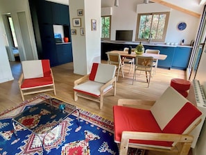 Ein modernes Wohnzimmer mit einem großen Teppich, Holzmöbeln und einer Küche im Hintergrund.