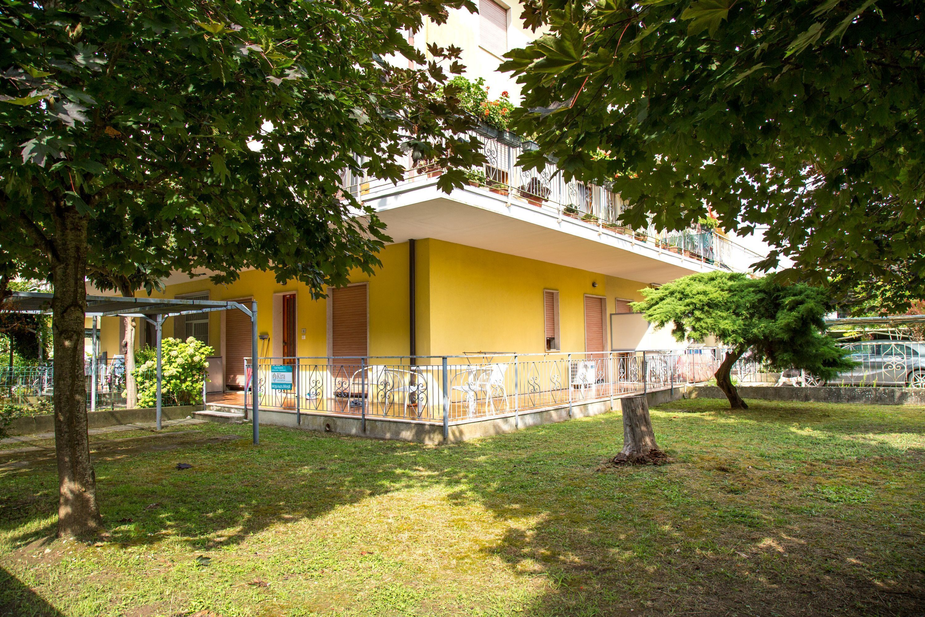 Un bâtiment jaune doté d’un balcon, entouré d’arbres et d’une clôture en métal.