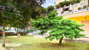 A tree-lined courtyard with a building featuring a balcony with potted plants. - Pinewood Escape With Garden (Eraclea)